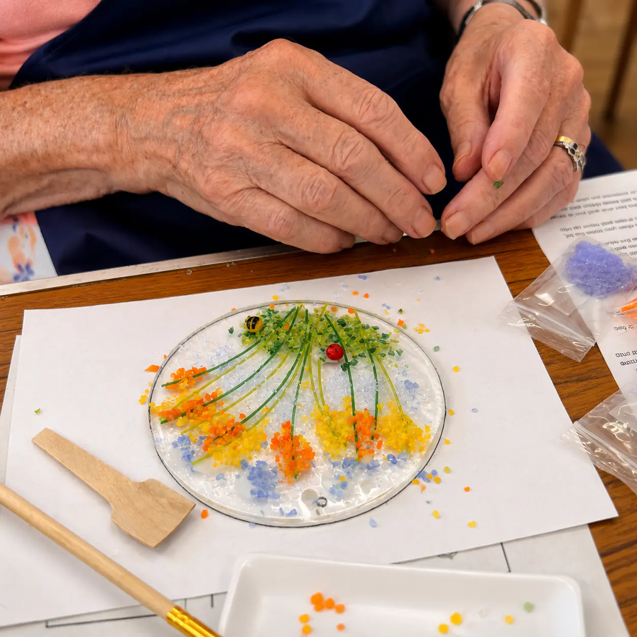 Hands arranging coloured glass frit into a floral fused glass design